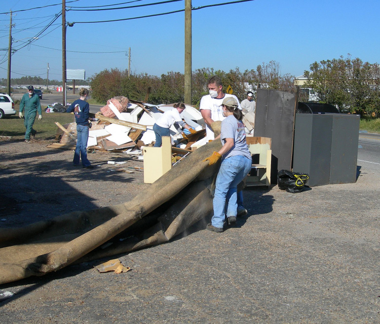 Several people pile debris next to a road.